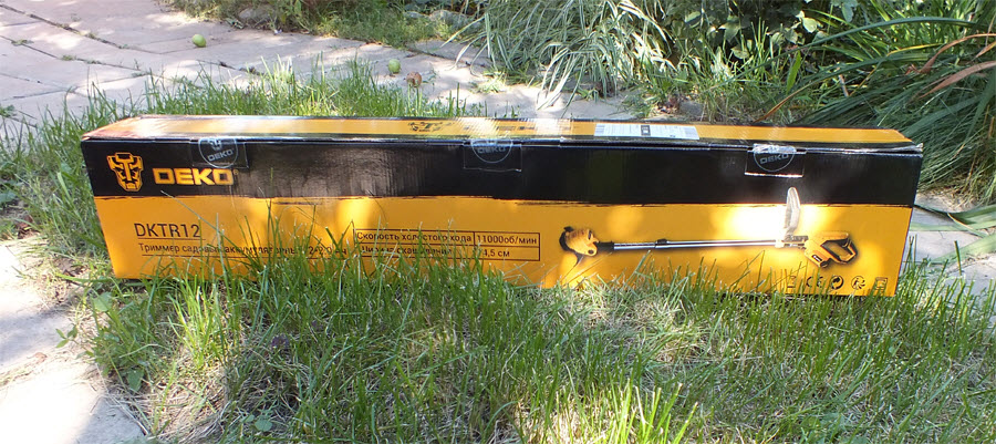 электрокоса DEKO DKTR12 в коробке на траве лужайки